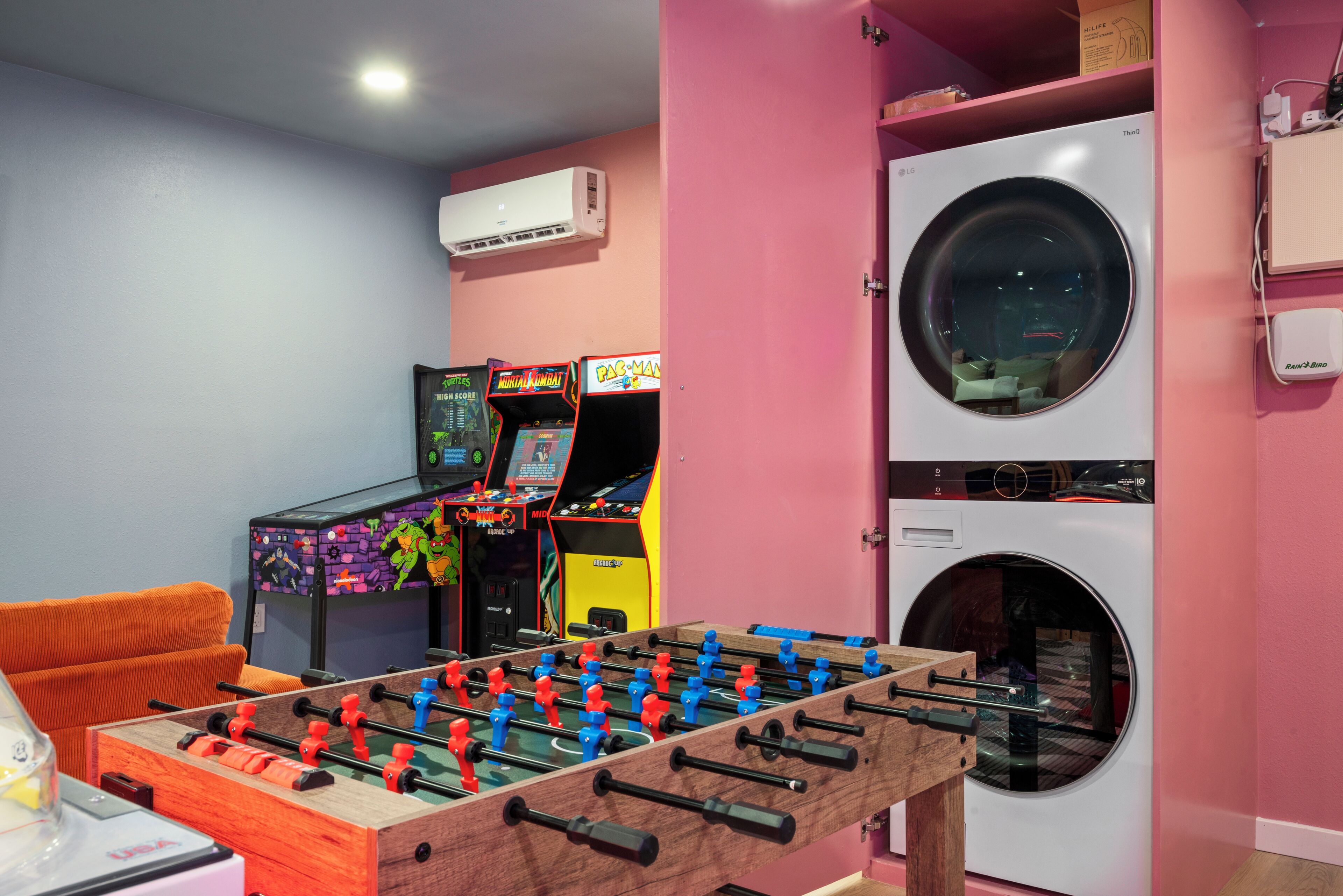 Una habitación con mesa de futbolín, juegos de arcade y lavadora.