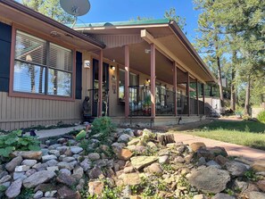 A building with a covered porch, large windows, and a stone pathway leading to the entrance. - Groovy View Cabin- Mountain Views W Covered Porch - Pet Friendly (Ruidoso)