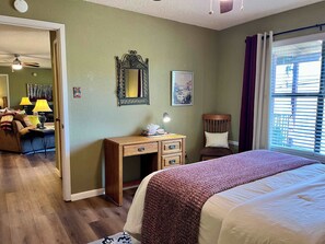 A hotel room with a bed, a desk with drawers, a chair, a lamp, a mirror, and a window with blinds. - Groovy View Cabin- Mountain Views W Covered Porch - Pet Friendly (Ruidoso)