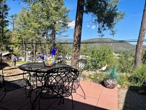 An outdoor patio with a metal table and chairs, surrounded by trees and a view of a mountainous landscape. - Groovy View Cabin- Mountain Views W Covered Porch - Pet Friendly (Ruidoso)