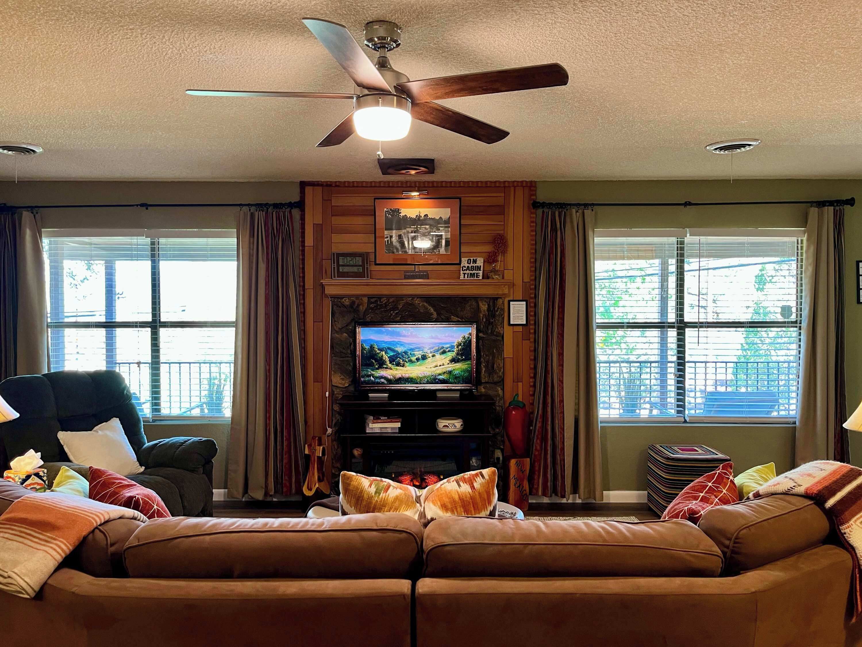 A living room with a television, a ceiling fan, and a fireplace.