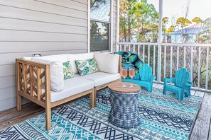 A covered porch with a white sofa, blue chairs, and a woven coffee table. - 4005 Rookery 3 Sea Story (Gulf Shores)
