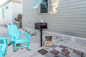 A backyard with a grill, a blue Adirondack chair, and a bag of wood chips. - 4005 Rookery 3 Sea Story two pools close to beach (Gulf Shores)