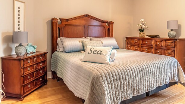 A bedroom with a wooden bed, a nightstand, a dresser, and a lamp. - 4005 Rookery 3 Sea Story (Gulf Shores)