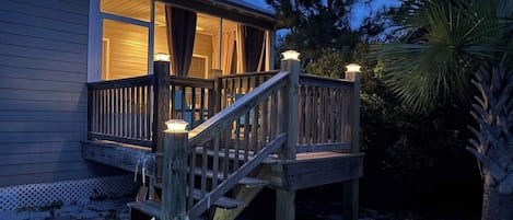 A wooden deck leading to a house with a porch and a staircase.