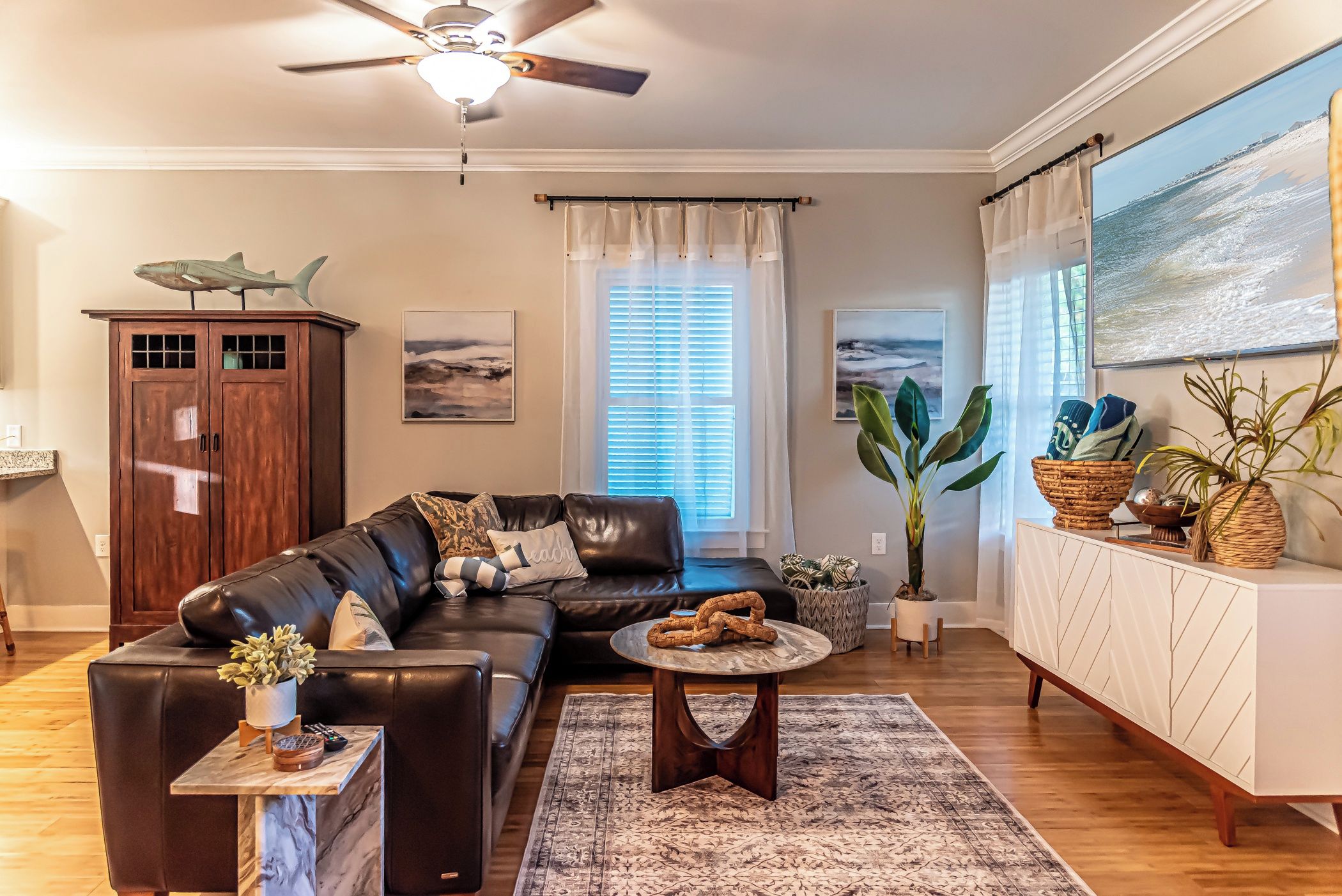A living room with a leather sofa, a coffee table, a cabinet, and a large window with blinds.