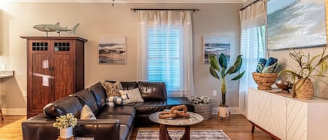 A living room with a leather sofa, a coffee table, a cabinet, and a large window with blinds.