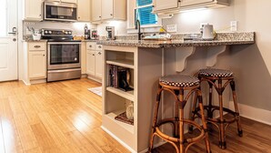 A kitchen with white cabinetry, stainless steel appliances, a granite countertop, and two wicker barstools. - 4005 Rookery 3 Sea Story (Gulf Shores)