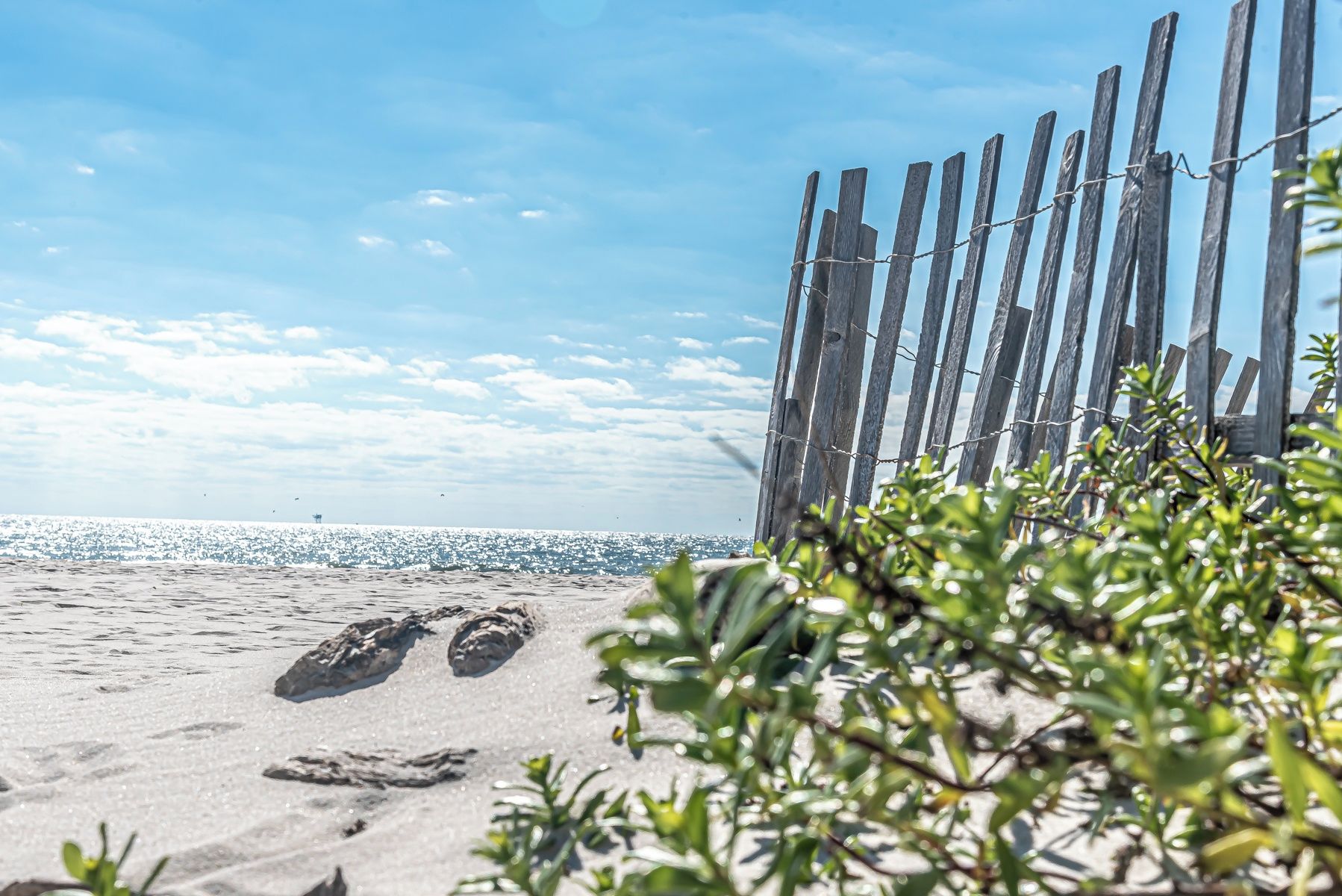 A sandy beach with footprints, a wooden fence, and a clear sky.
