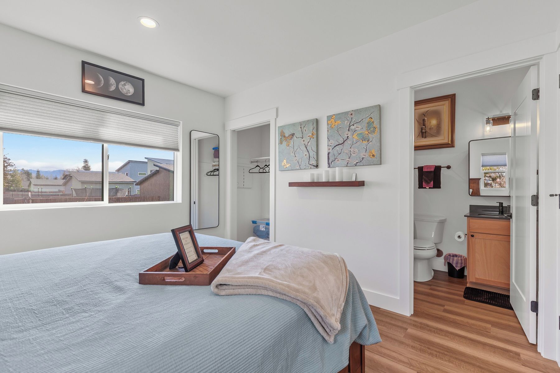 A bedroom with a bed, a window, a mirror, and artwork on the wall.
