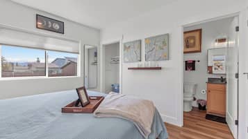 A bedroom with a bed, a window, a mirror, and artwork on the wall.