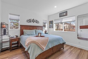 Ein Schlafzimmer mit einem hölzernen Bett, einem Nachttisch, einer Wanddekoration und einem Fenster mit Jalousien.