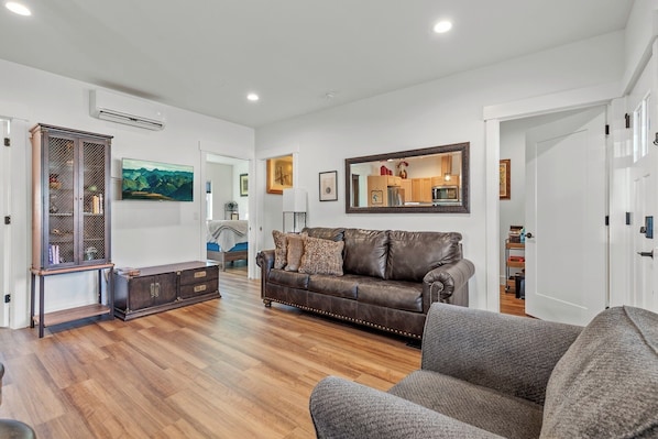 Una sala de estar con un sofá de cuero marrón, un sillón gris y un aparador de madera.