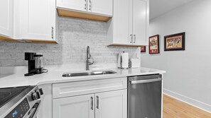 A modern kitchen with white cabinets, a stainless steel sink, a coffee maker, and a dishwasher.
