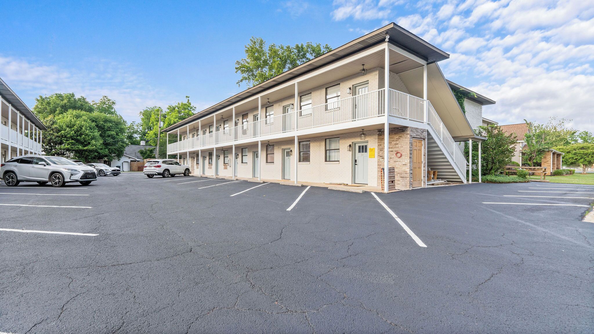 A multi-story motel with a parking lot, a covered outdoor area, and a staircase leading to the upper floors.