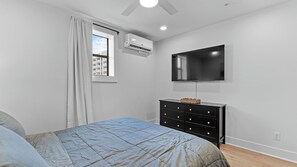 A bedroom with a bed, a dresser, a television, and an air conditioning unit.