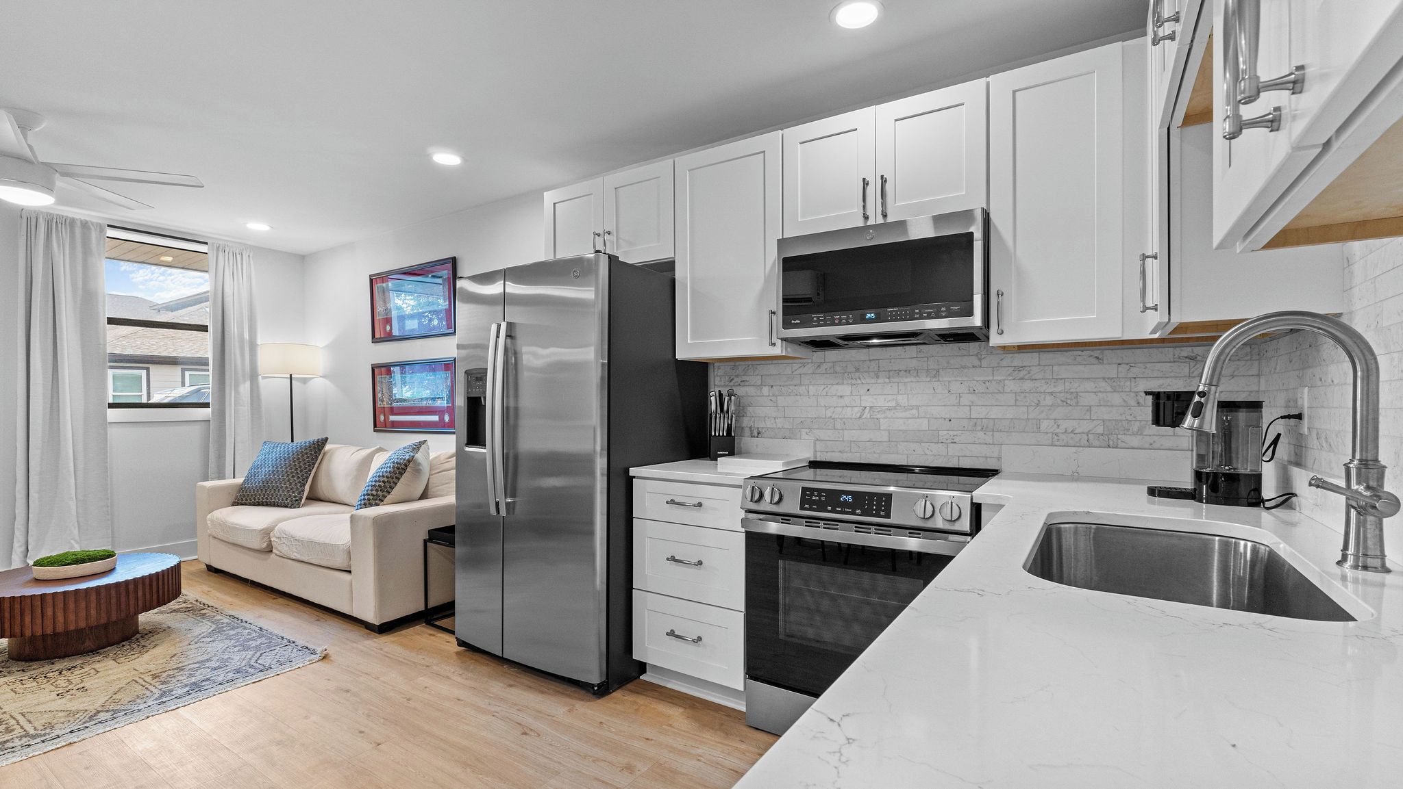 A modern kitchen with white cabinetry, a stainless steel refrigerator, an oven, and a microwave.