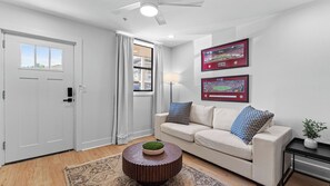 A modern living room with a beige sofa, a round coffee table with a green centerpiece, and two framed sports photographs on the wall.