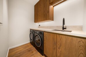 A compact kitchen with wooden cabinetry, a built-in washing machine, and a sink. - Villa Frogmore (Queenstown)
