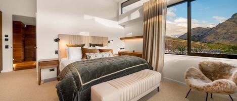A modern bedroom with a large bed, a bench, a chair, and a view of mountains through a window.