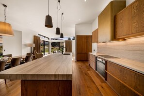 A modern kitchen with a central island, wooden cabinetry, and pendant lighting. - Villa Frogmore (Queenstown)