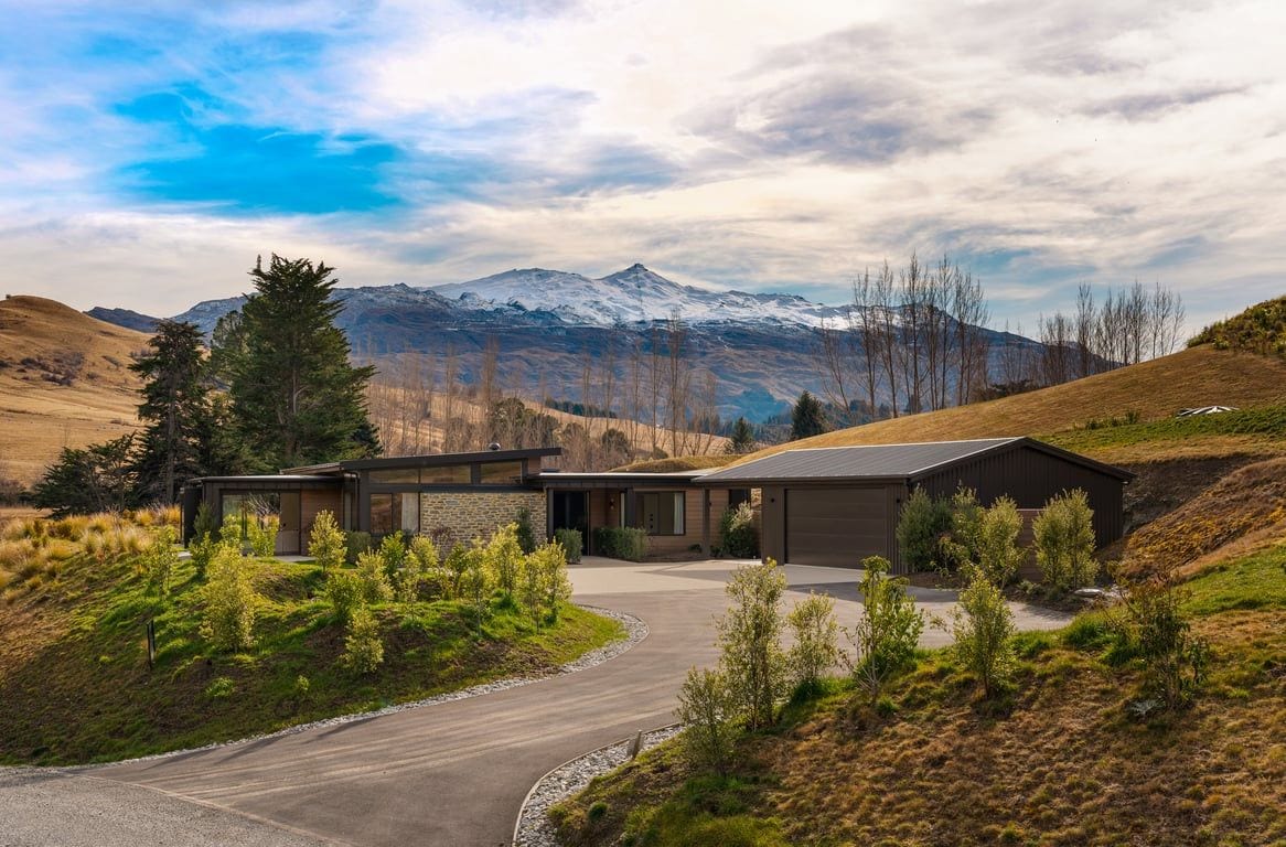A modern two-story house with a garage, surrounded by a landscaped driveway and a mountain backdrop.