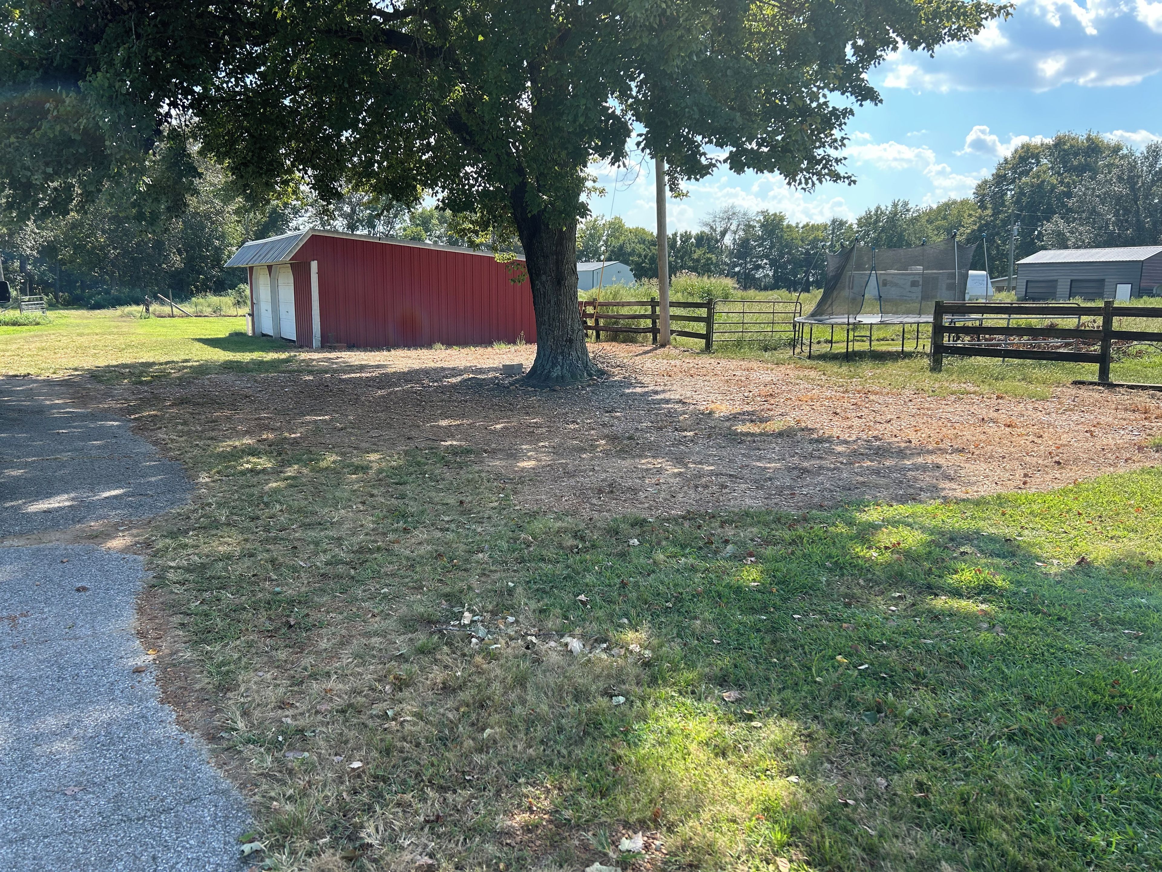 A rural landscape with a red barn, a fenced area, and a tree.