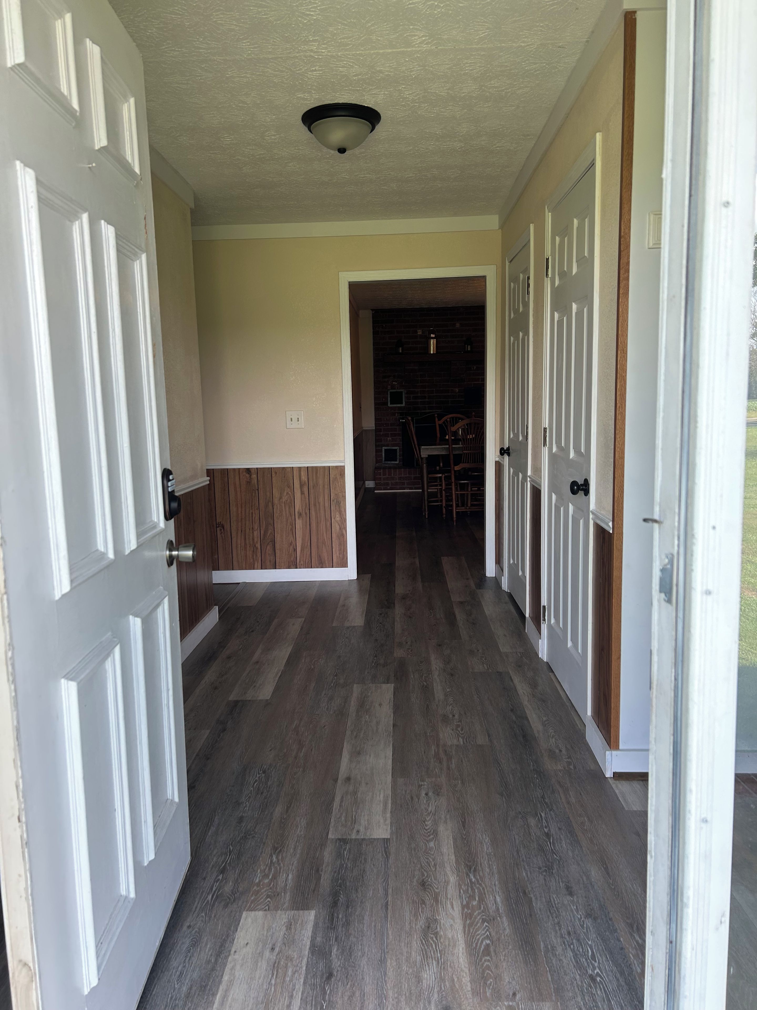 Un couloir avec un plancher en bois, des portes blanches et un mur en briques.