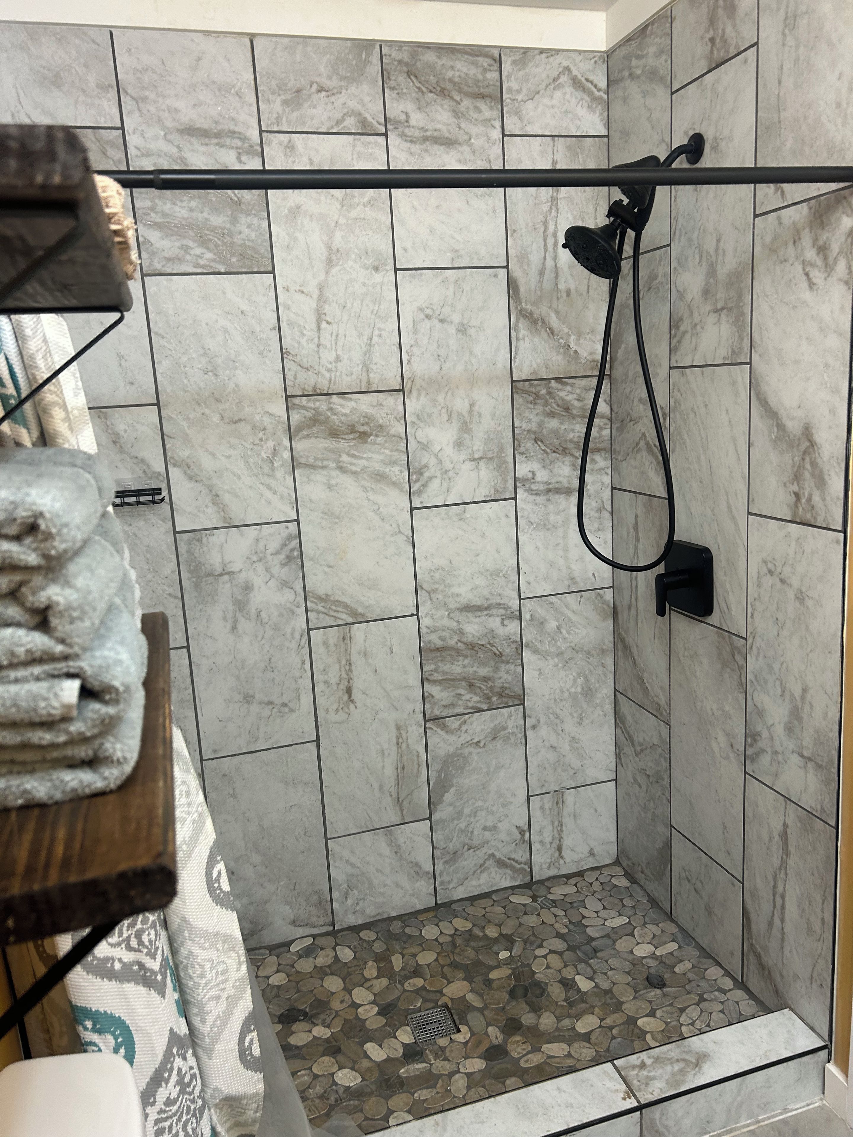 A shower area with a tiled wall, a handheld showerhead, and a floor with pebble tiles.