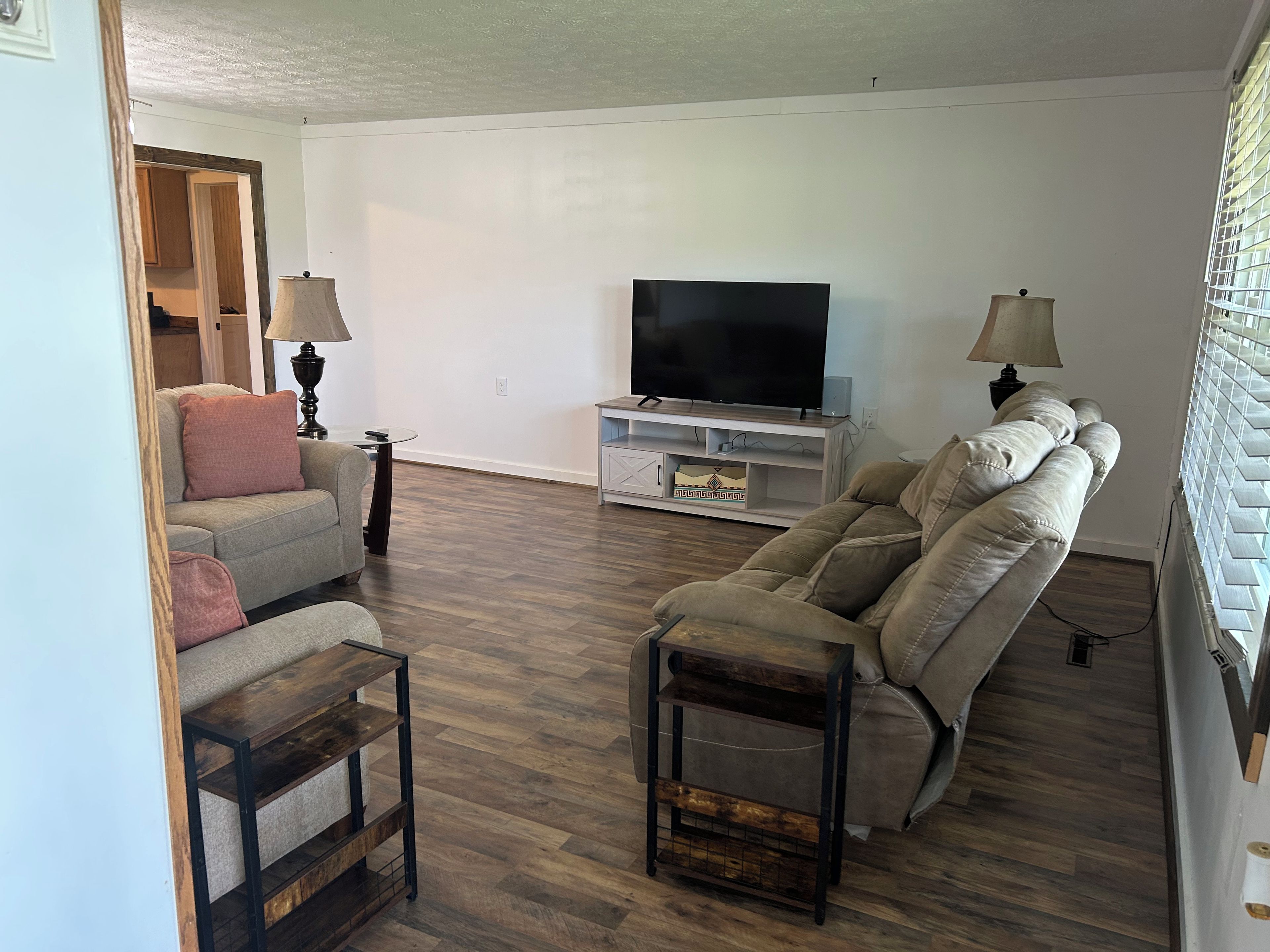 Una sala de estar con sofá, sillón reclinable, mueble para televisión y lámpara.