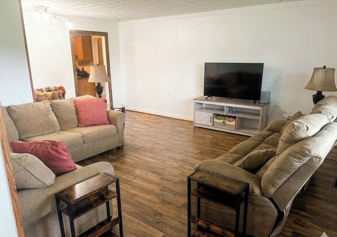 Una sala de estar con un sofá, un sillón reclinable, un televisor sobre un mueble bajo y una lámpara.