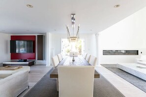 Un espace de salle à manger moderne avec une longue table, des chaises blanches et un lustre.