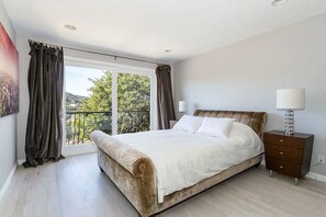 Une chambre à coucher avec un grand lit, une table de chevet, une lampe et une vue par la fenêtre.