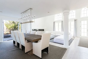 Ein geräumiges Zimmer mit Essbereich, ausgestattet mit einem Holztisch, weißen Stühlen, einer Couch und einem großen Fenster, das für natürliches Licht sorgt.