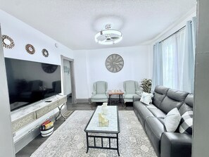 A modern living room with a flat-screen TV, two armchairs, a sofa, a coffee table, and a large wall clock. - 3BR Home 15 Min to AirPort, 10 min Stadiums & More (Minneapolis)