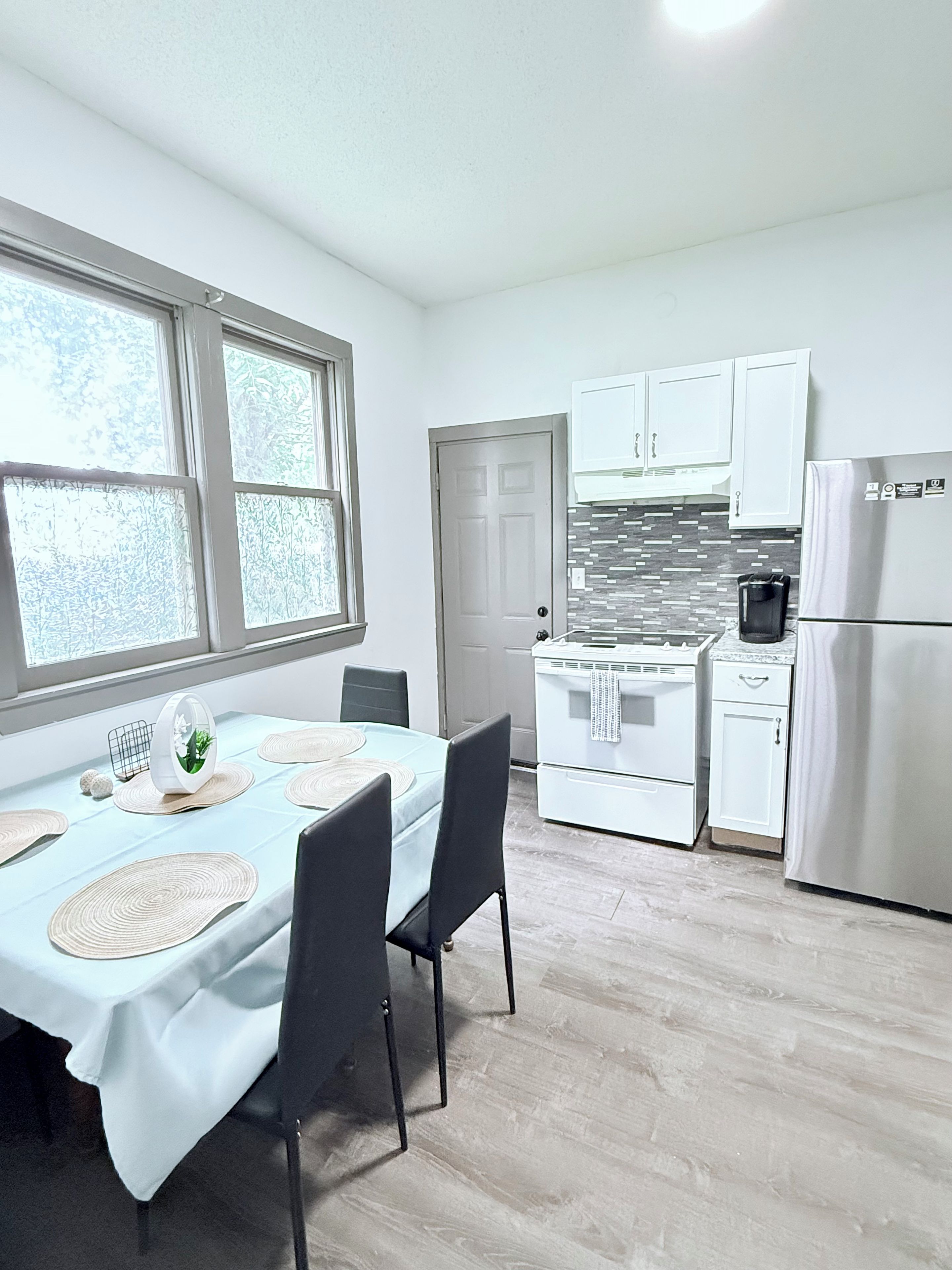 A modern kitchen with white cabinets, a stainless steel refrigerator, and a dining area with a table set for four.