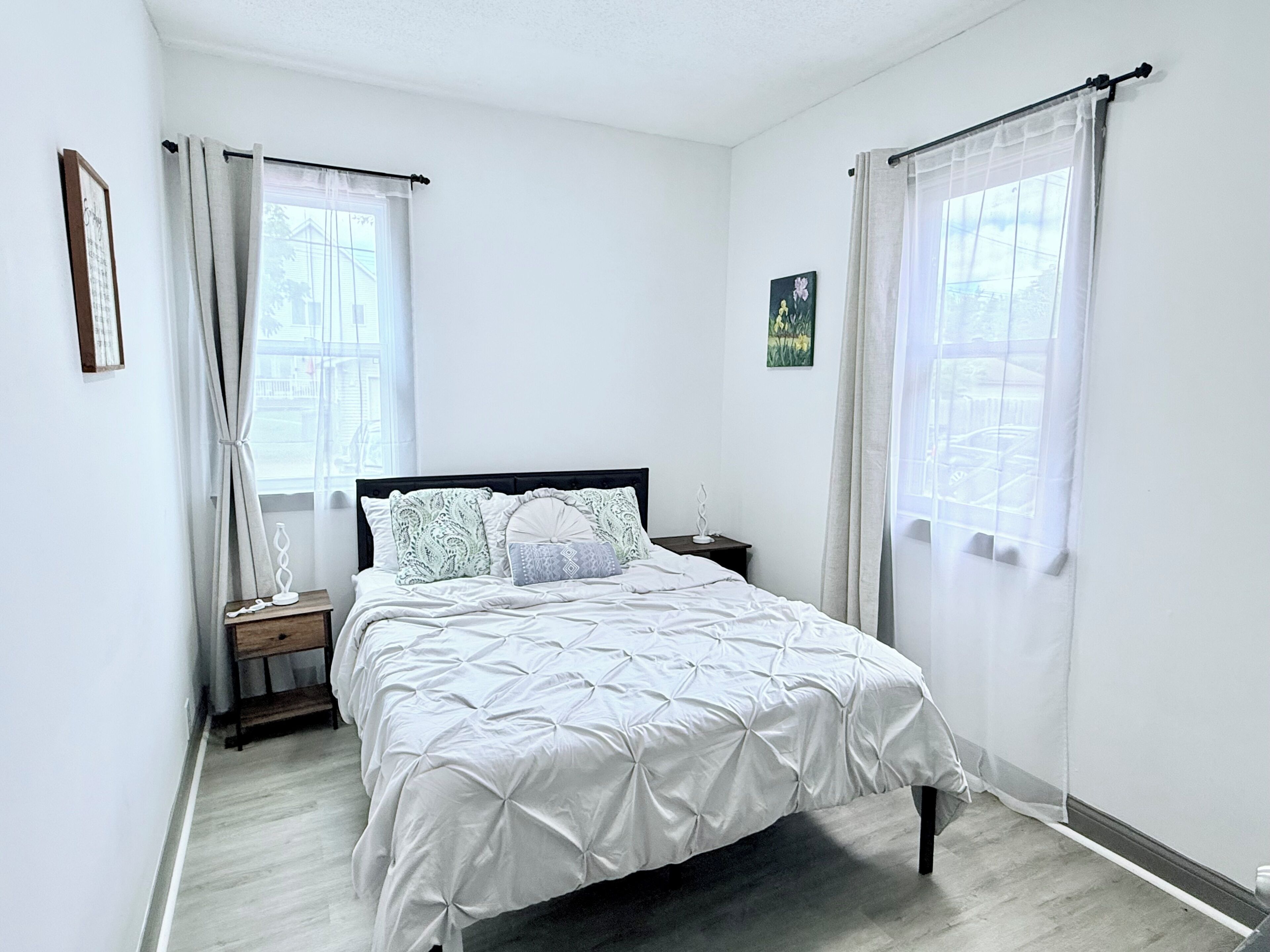 A bedroom with a bed, curtains, a nightstand, and a picture on the wall.