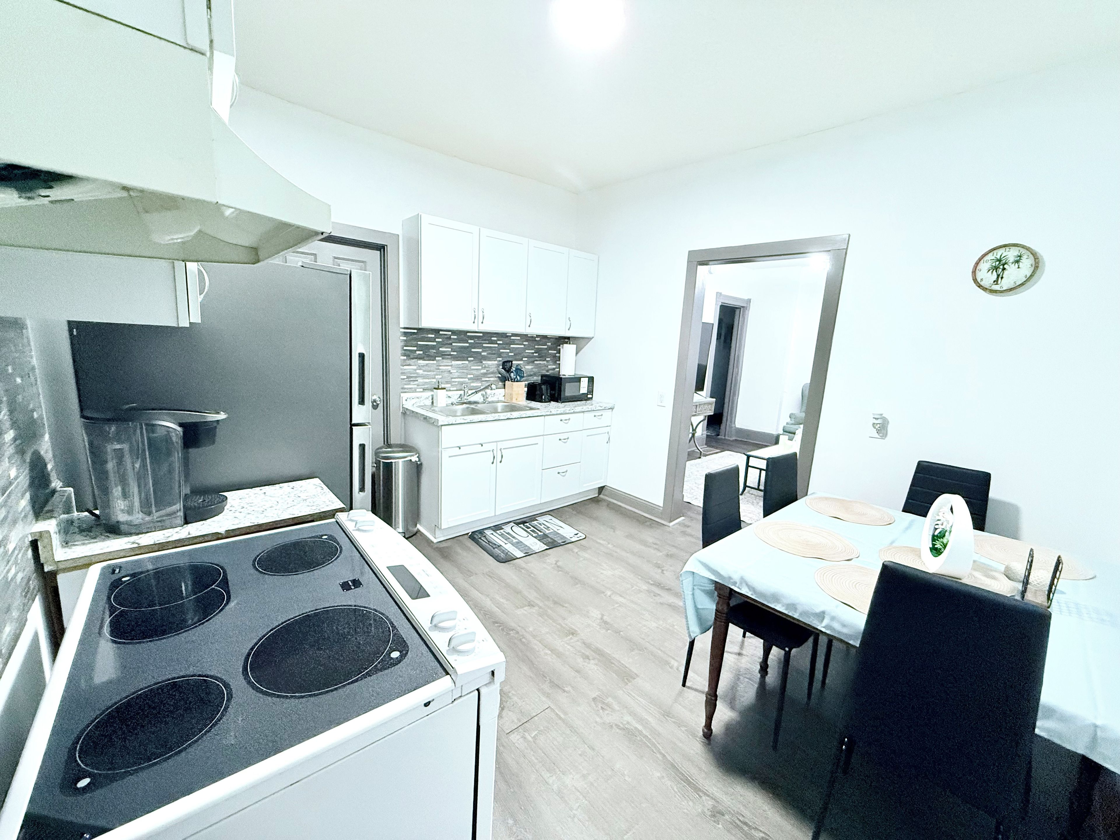 Une cuisine moderne équipée d’une cuisinière, d’un évier et de meubles blancs. On y trouve également un coin repas avec une table et des chaises.