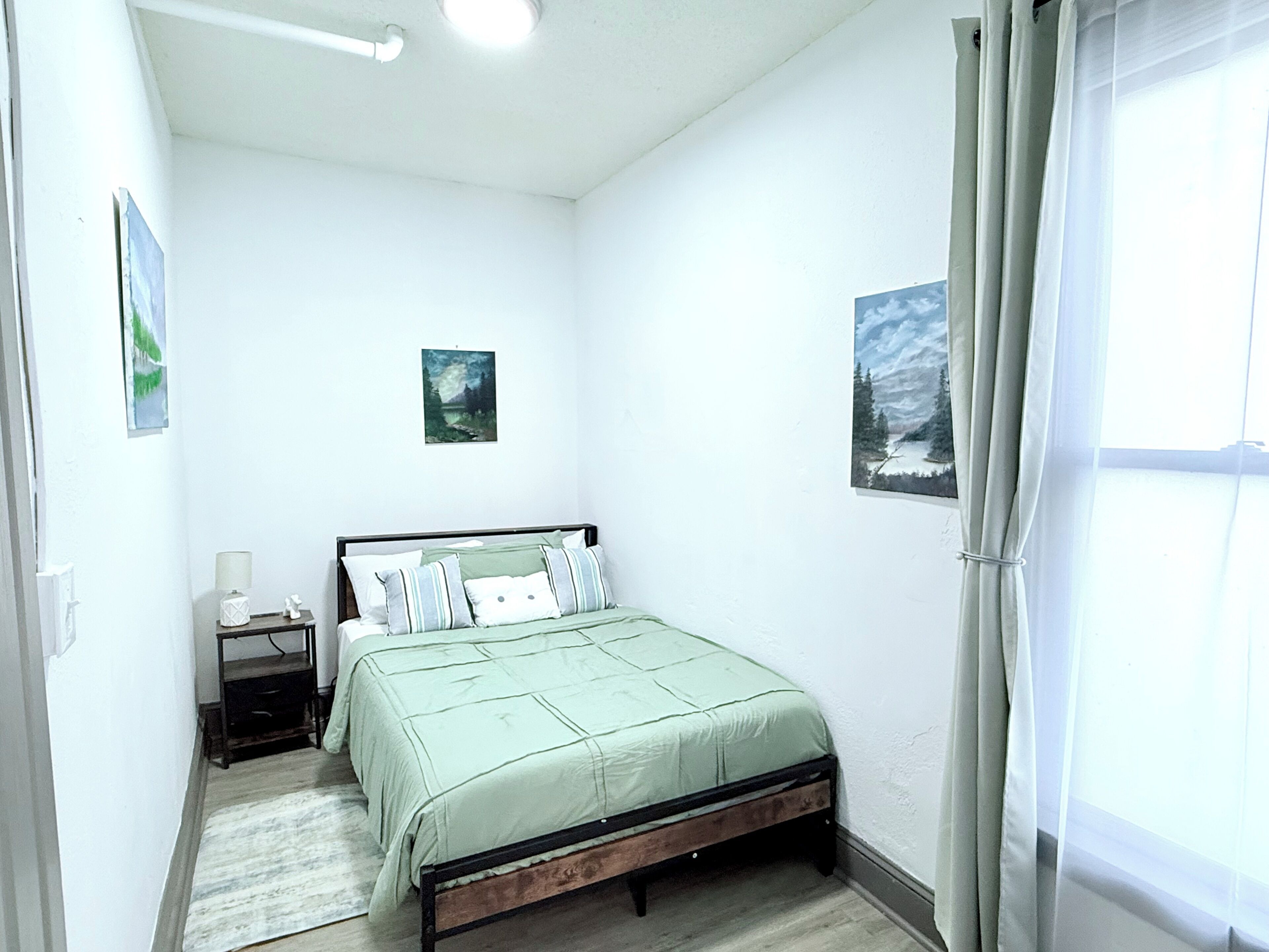 A bedroom with a bed, a nightstand, a lamp, and two paintings on the wall.