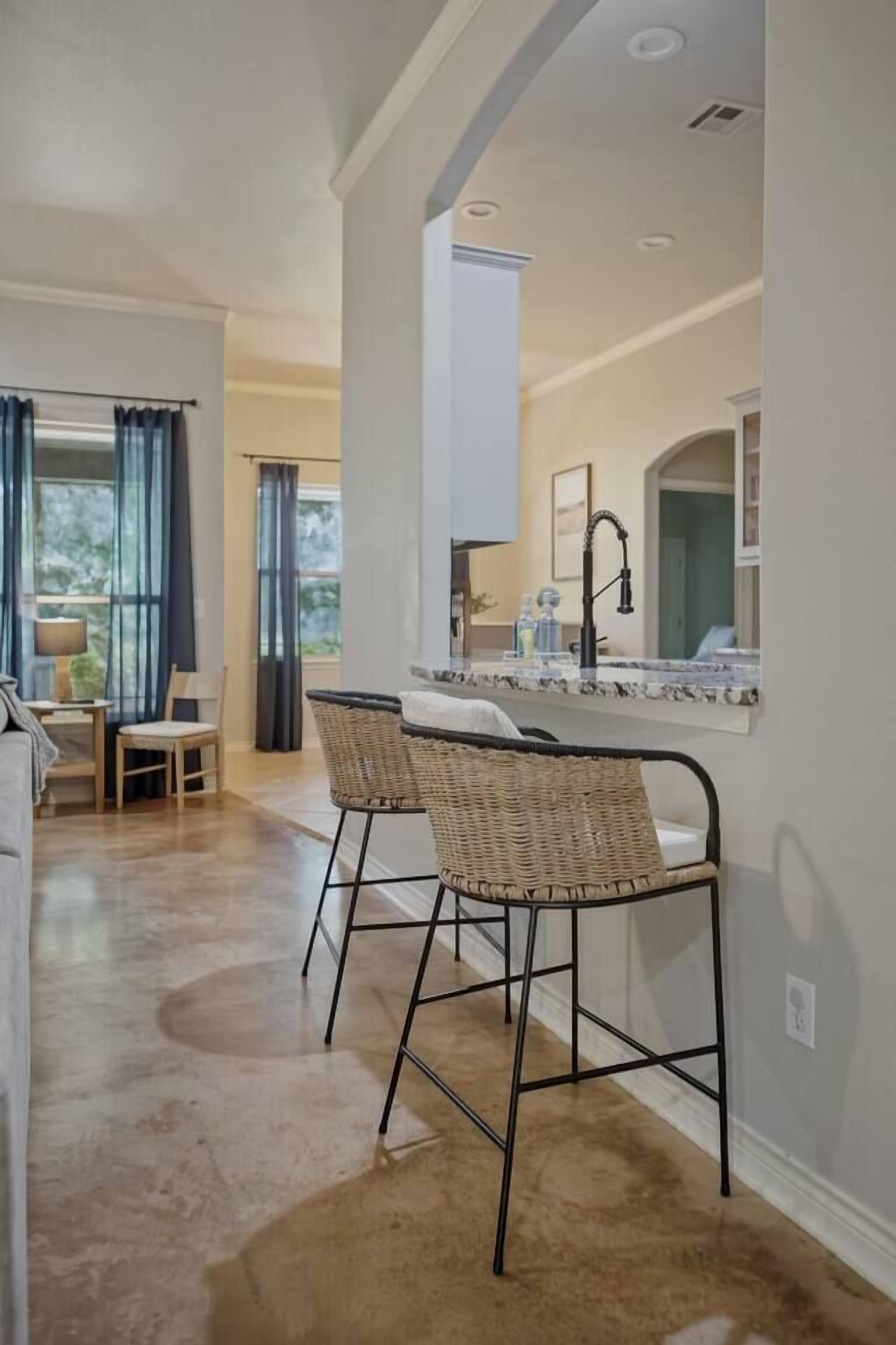 A modern kitchen with a bar area, two wicker chairs, and a large window.