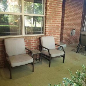 Dos sillones con cojines, una mesita y una pared de ladrillo con una ventana.