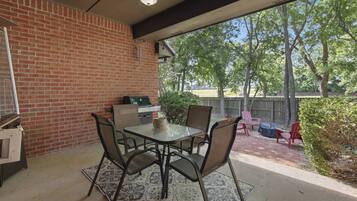 Un patio con pared de ladrillo, una parrilla y una mesa con sillas.