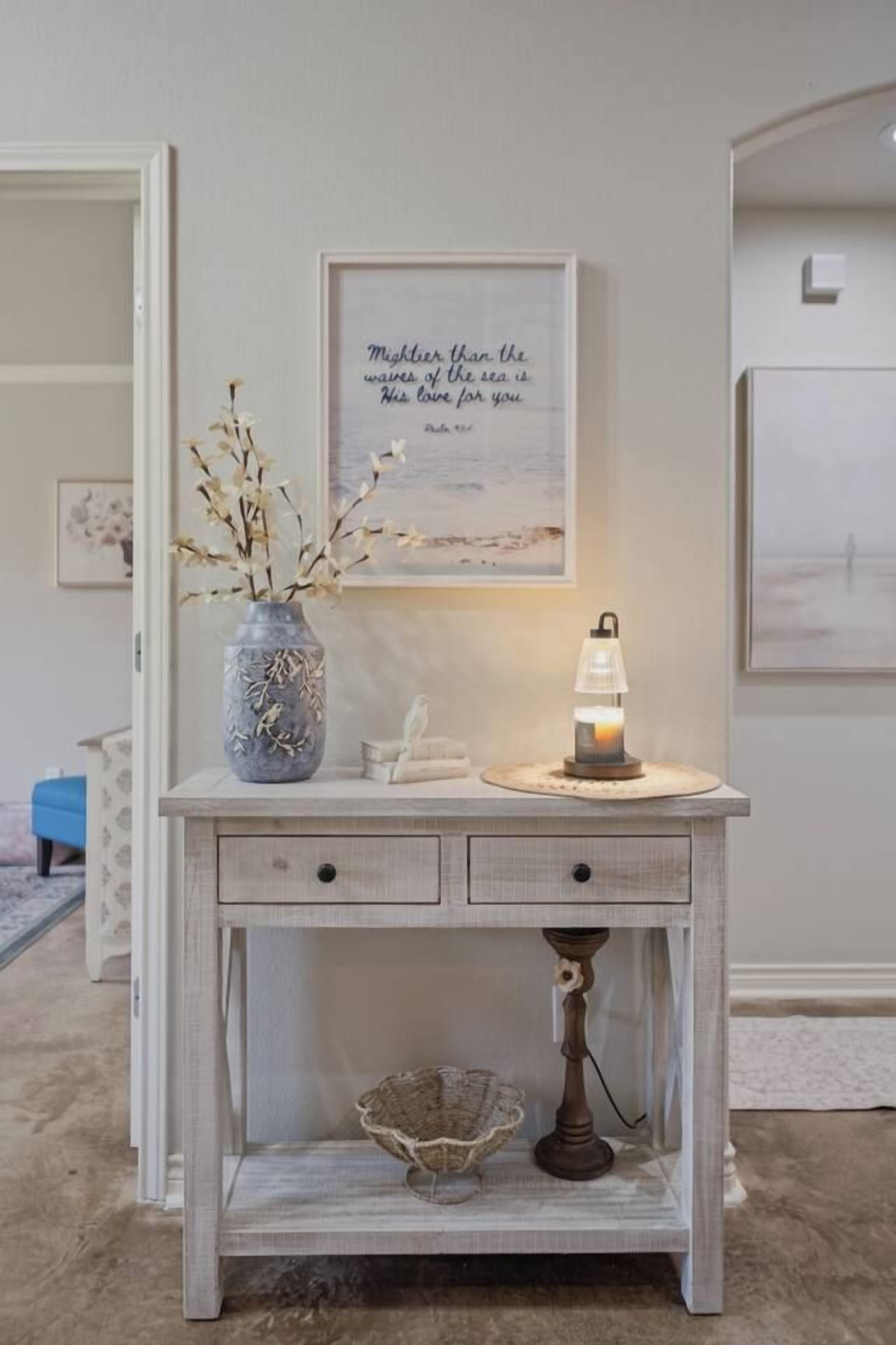A white console table with a vase, a candle, and a framed quote.
