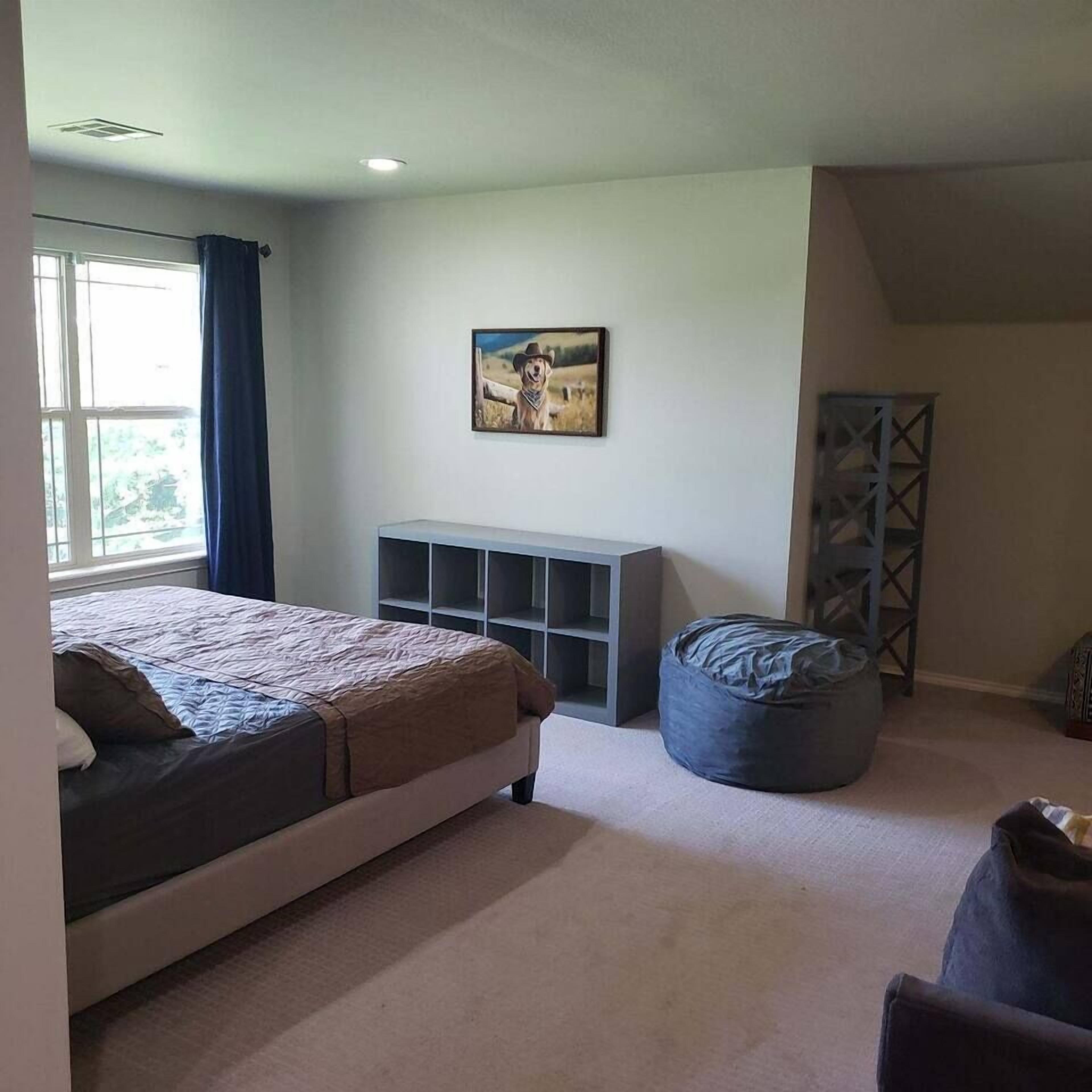 Une chambre à coucher comprenant un lit, une banquette intégrée, une étagère fixée au mur et une fenêtre avec des rideaux.