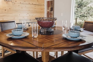 A round wooden dining table with a central decorative bowl, surrounded by matching blue bowls and clear glasses. - Dixon Cove Lookout Near Horsetooth Res (Fort Collins)