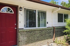 Une maison avec une porte rouge, portant le numéro 215, et deux fenêtres aux cadres blancs.