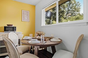 Un coin repas avec une table ronde dressée pour quatre personnes, un four à micro-ondes posé sur le comptoir et une fenêtre donnant sur les arbres.