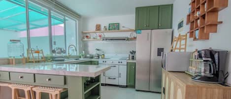 A kitchen with a central island, a stove, refrigerator, and wooden shelves.