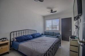 A bedroom with a bed, a nightstand, a desk, a chair, a window, and a door.