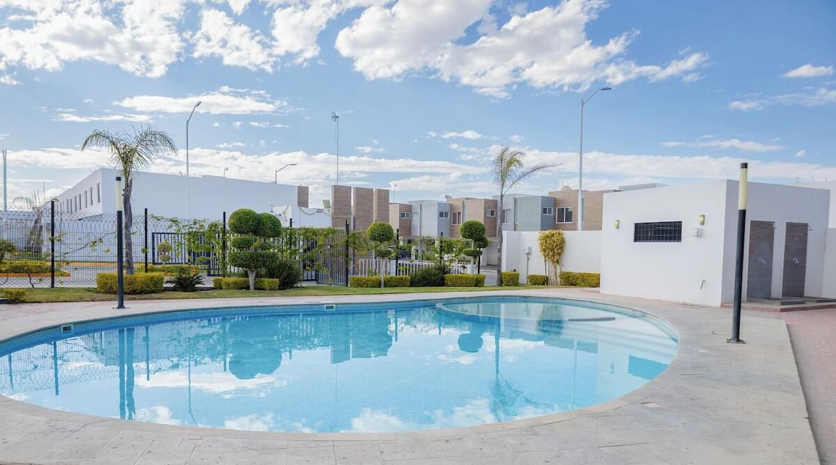 A swimming pool surrounded by modern buildings, a clear sky, and well-maintained landscaping.